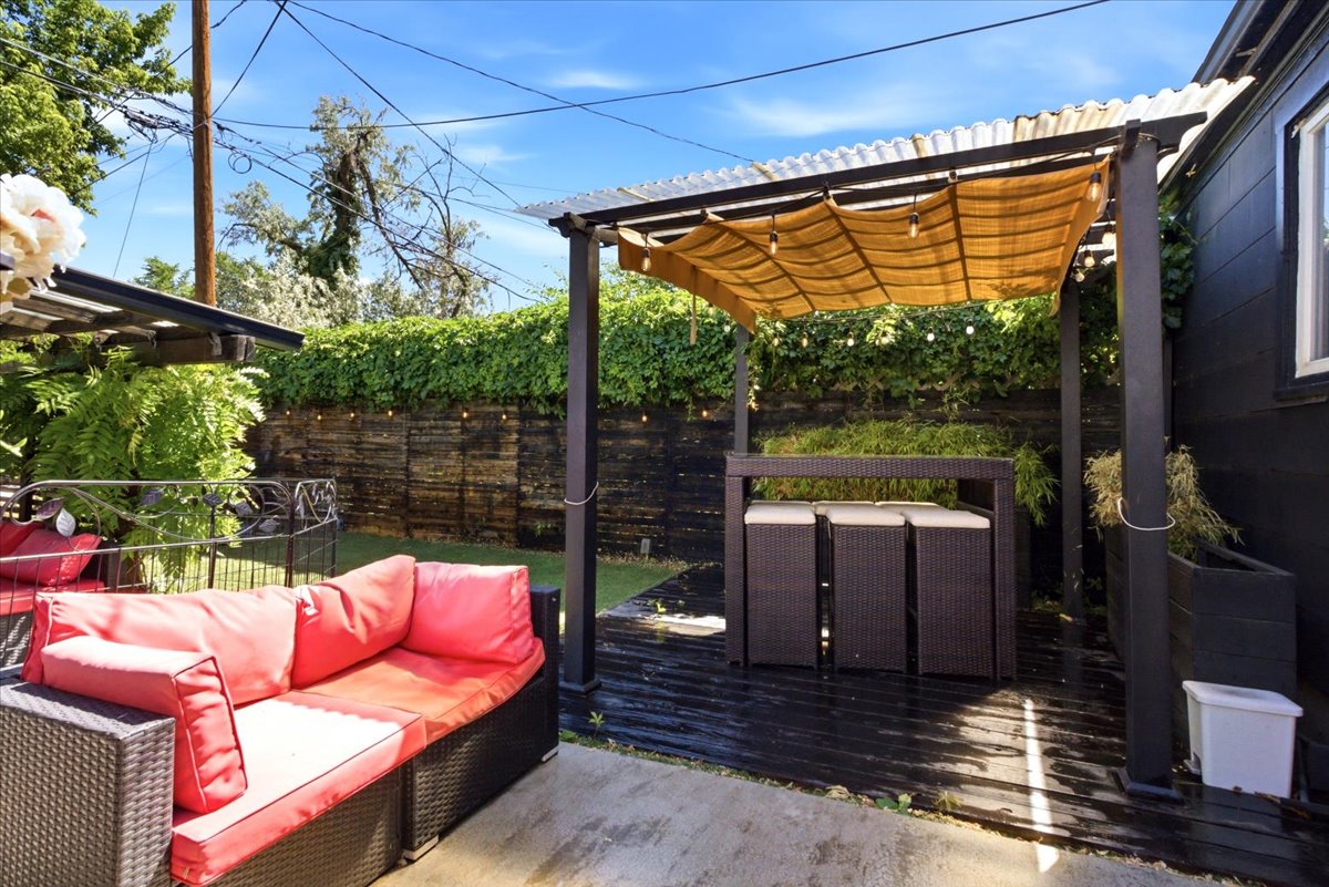 Outdoor living area featuring a covered patio, wood-finish decking, and a privacy fence with established greenery