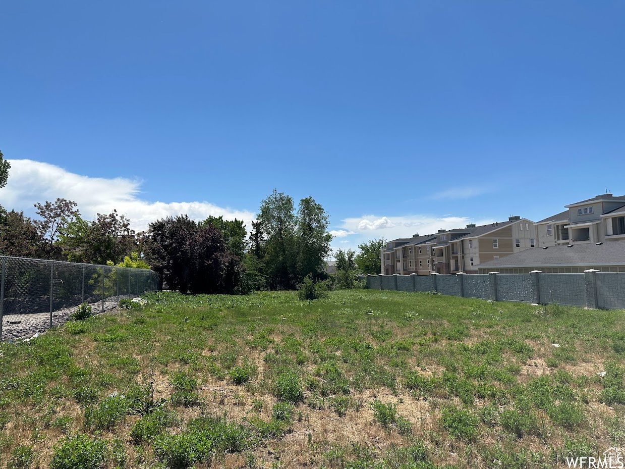 Expansive lot featuring natural ground cover, mature trees, chain-link fencing, and a decorative block wall