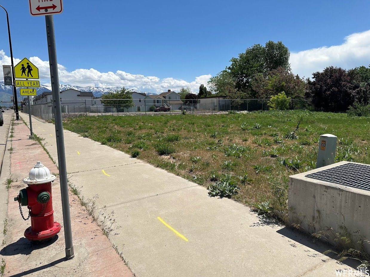 Expansive undeveloped lot featuring a concrete sidewalk and mature trees in the background