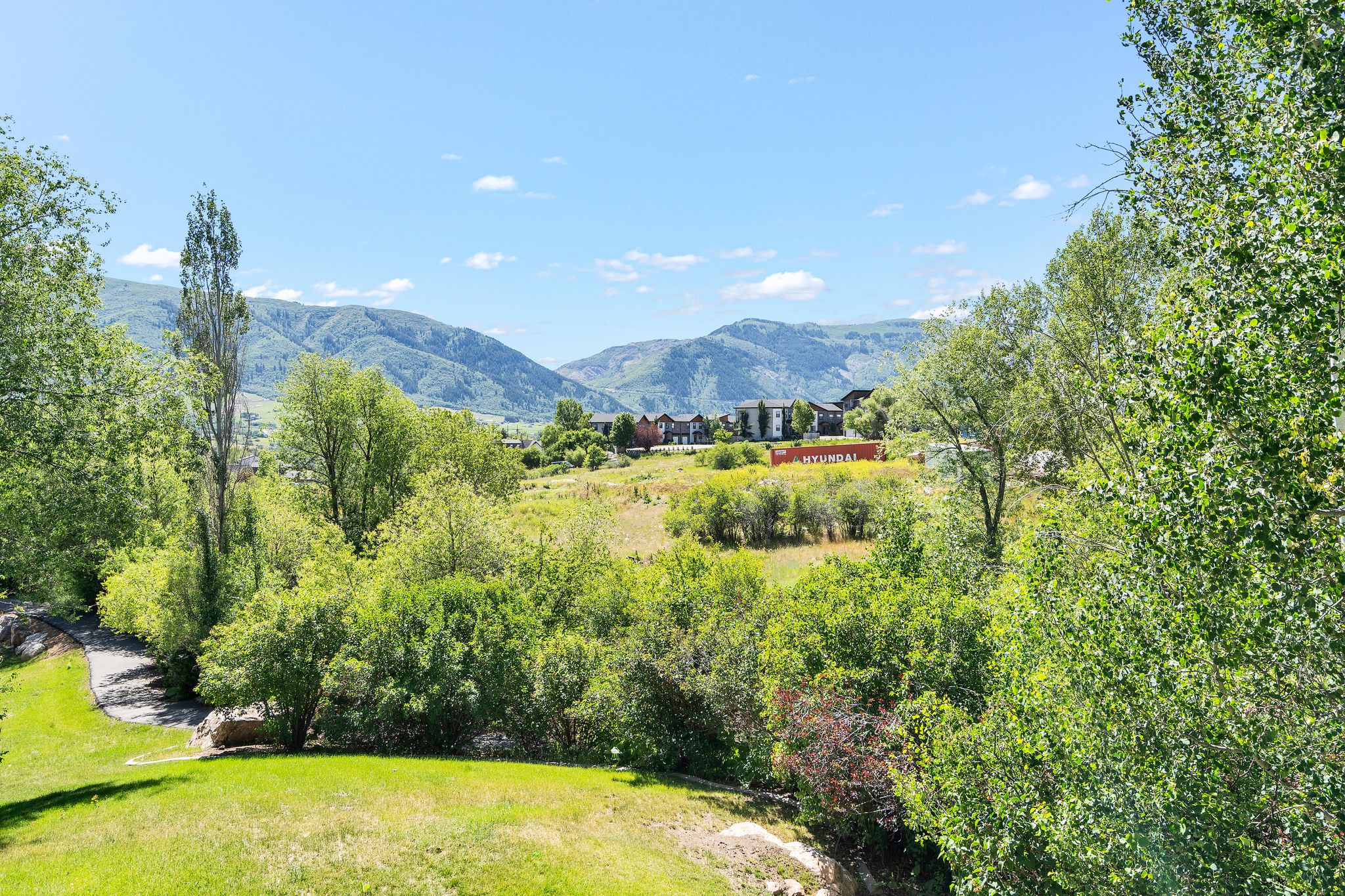 Expansive outdoor grounds featuring a rolling lawn and mature trees, surrounded by distant mountains