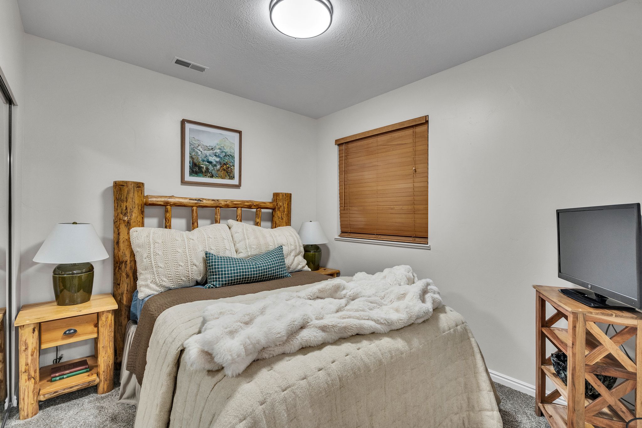 Bedroom featuring neutral wall paint, a window with wood-finish blinds, and a ceiling-mounted light fixture