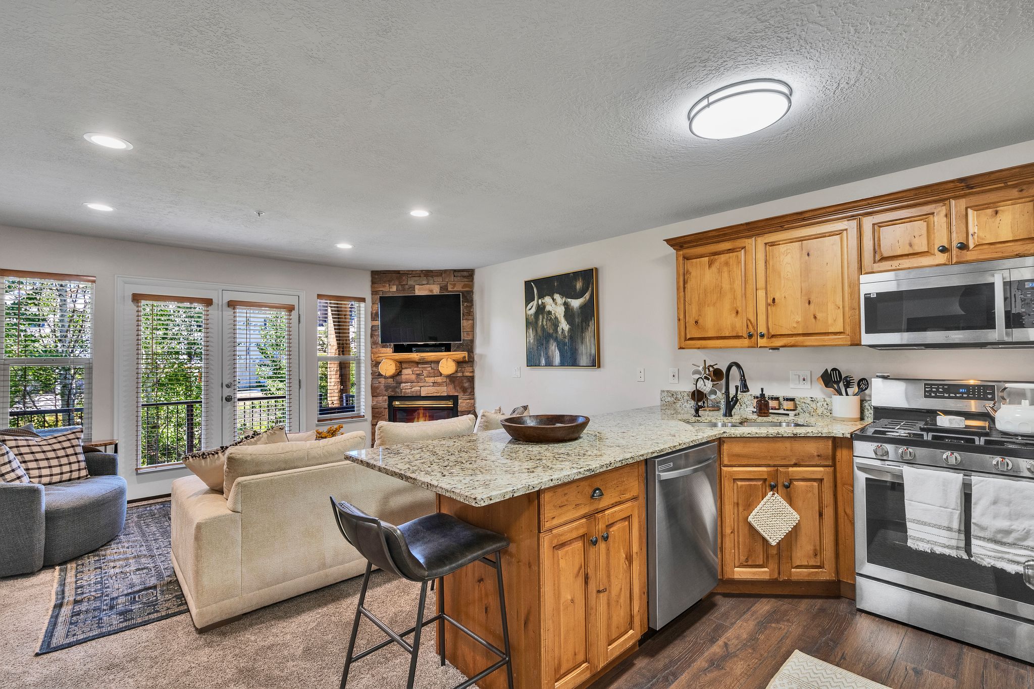 Open-concept kitchen and living area featuring wood-finish flooring, granite countertops, and stainless steel appliances