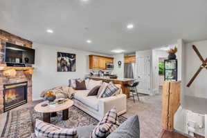 Open-concept living space featuring a stacked stone fireplace with a log mantel, recessed lighting, and soft gray carpeting