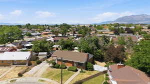 Aerial perspective of a neighborhood featuring multiple residential properties with pitched roofs, mature trees, and mountain scenery in the distance