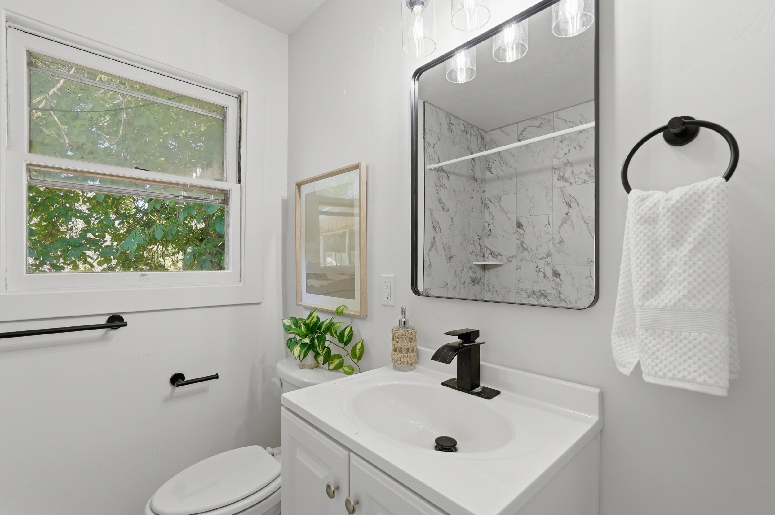 Bathroom featuring a white vanity with integrated sink, black hardware, framed mirror, and window