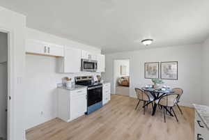 Kitchen and dining area featuring white cabinetry, stainless steel microwave, black range, and light wood-finish flooring