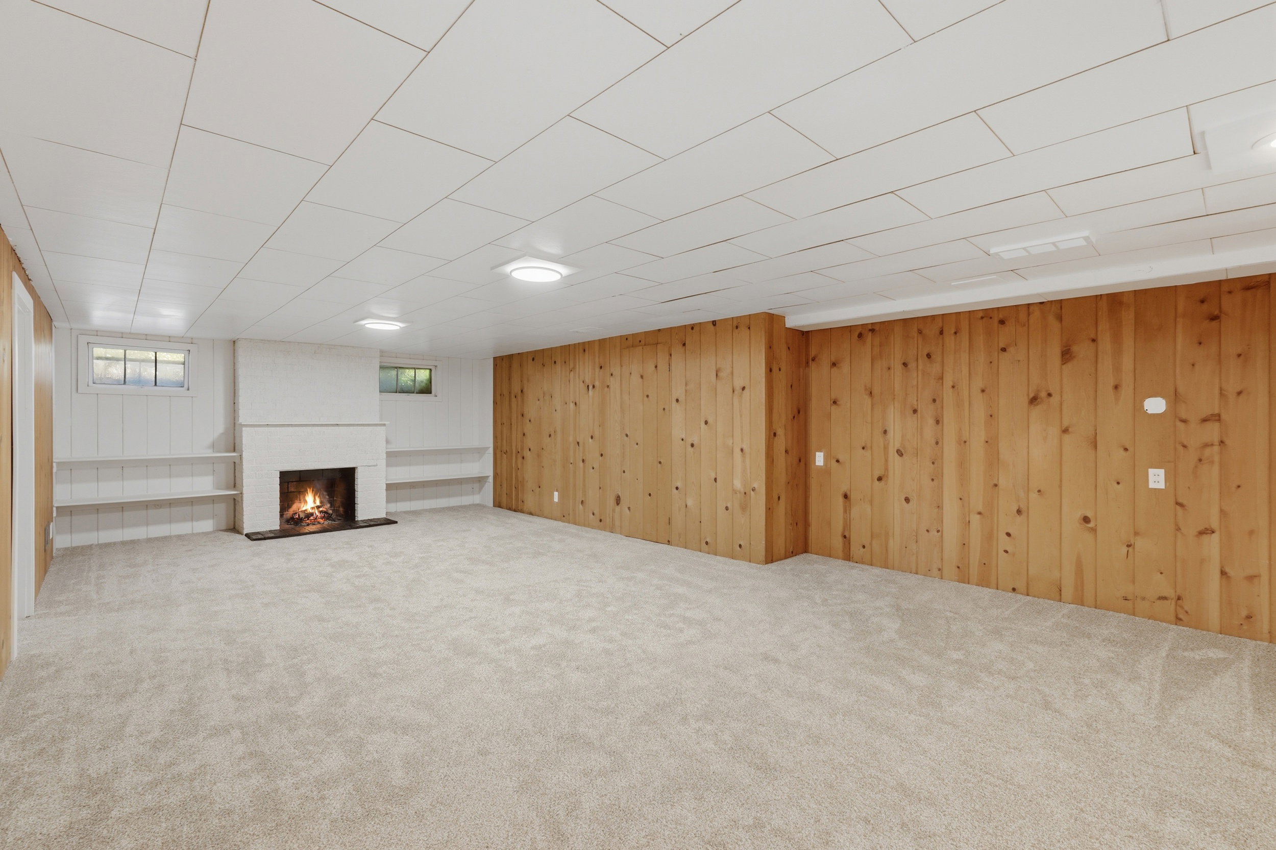 Spacious room featuring a central white fireplace, light-toned carpeting, and wood paneling on one wall