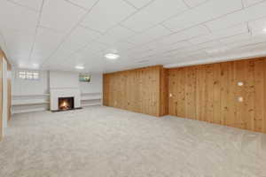 Spacious room featuring a central white fireplace, light-toned carpeting, and wood paneling on one wall
