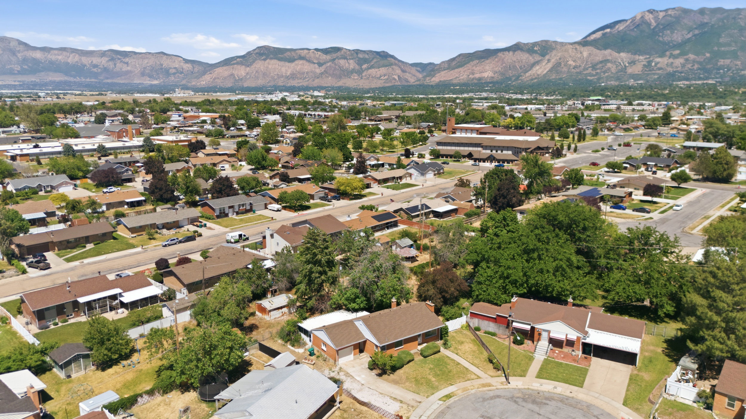 Residential neighborhood featuring single-story homes with pitched roofs, mature trees, and mountainous terrain in the background