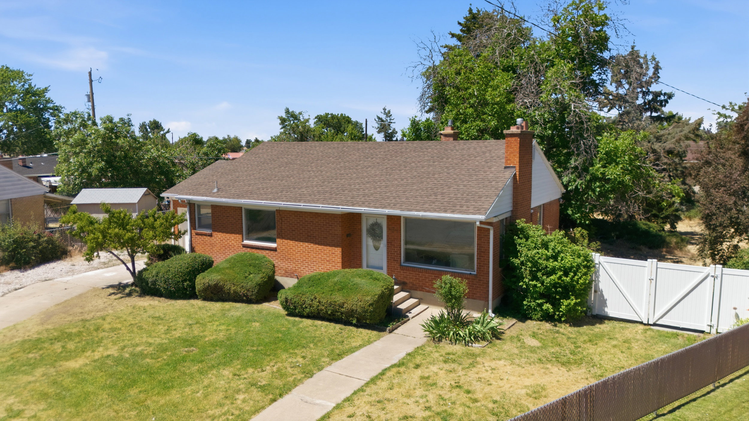 Red brick ranch-style home featuring a brown shingle roof, established landscaping, and a concrete pathway leading to the front entry