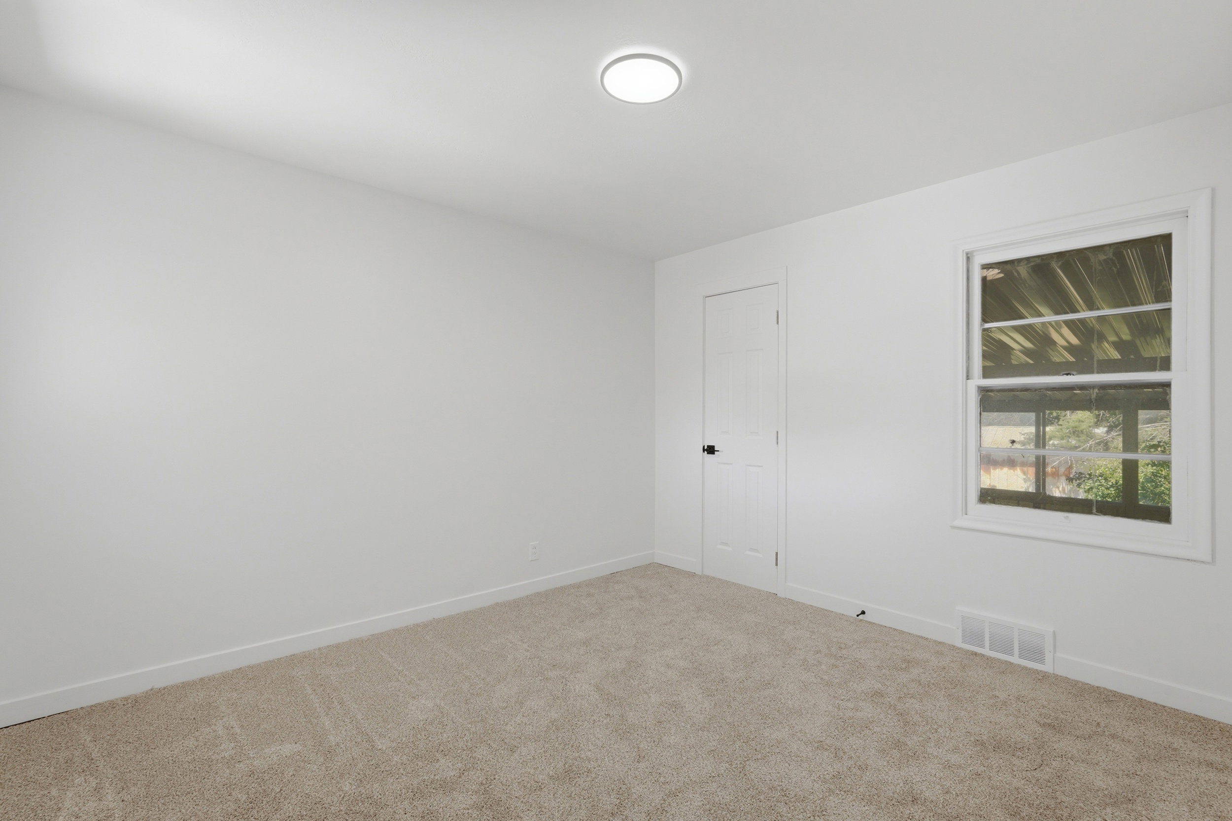 Carpeted room featuring a white paneled door with matte black hardware, a double-hung window, and a ceiling-mounted flush light fixture