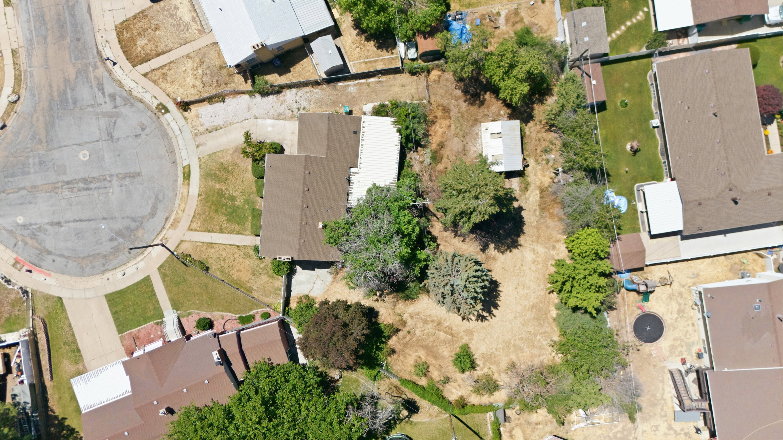 Cul-de-sac property featuring a brown shingle roof, mature trees, and a detached shed