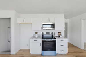 Contemporary kitchen featuring white cabinetry, stainless steel appliances, granite-style countertops, and wood-finish flooring