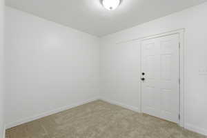 Room featuring light-toned carpeting, white walls, and a white six-panel door with matte black hardware