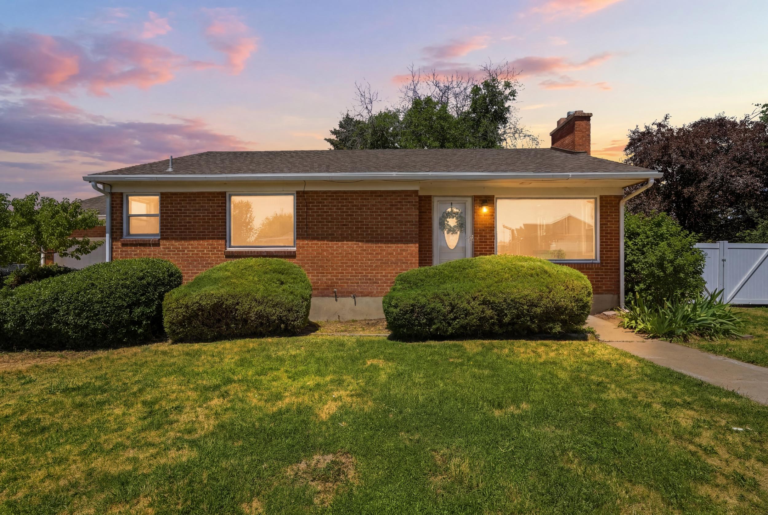 Brick exterior with a gabled roofline, front lawn, and mature shrubbery
