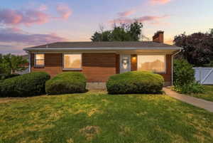 Brick exterior with a gabled roofline, front lawn, and mature shrubbery