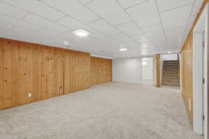 Spacious room featuring light-colored carpeting, wood paneling, white walls, and a white tile ceiling with recessed lighting