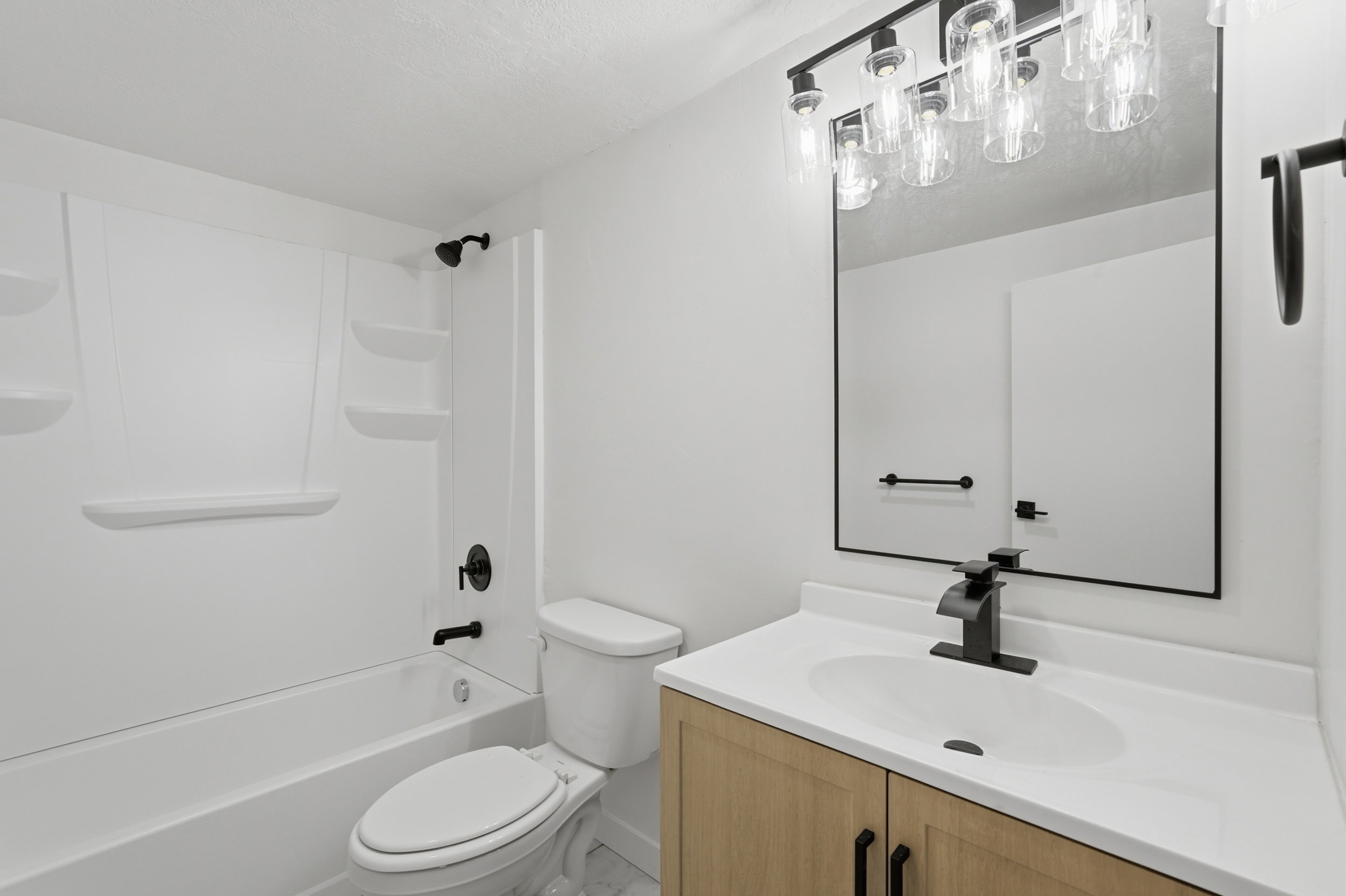 Bathroom featuring a light wood-finish vanity with a white countertop and undermount sink, matte black faucet, and a large framed mirror