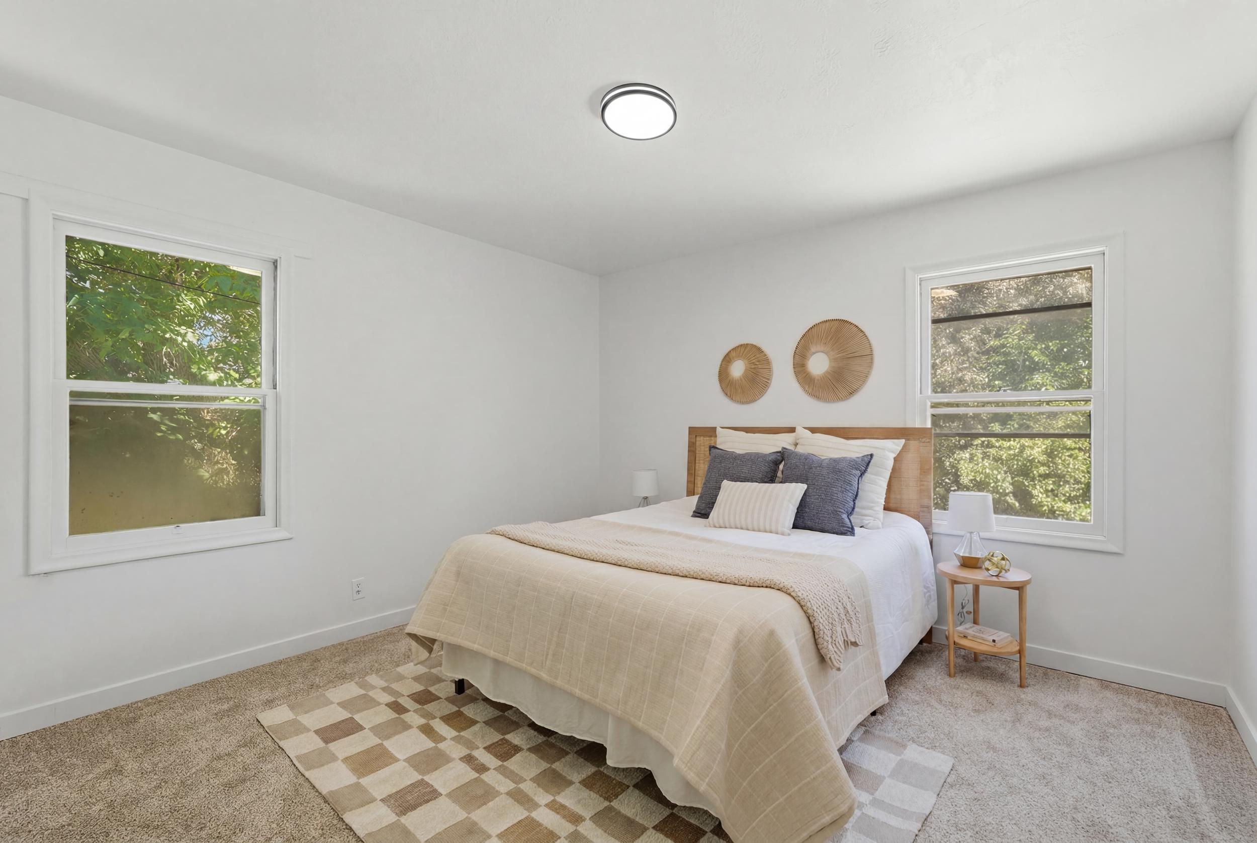 Bright bedroom featuring two large windows, white walls, light-toned carpeting, and a flush-mount ceiling light fixture