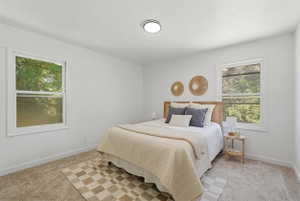 Bright bedroom featuring two large windows, white walls, light-toned carpeting, and a flush-mount ceiling light fixture