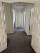 Hallway featuring neutral-toned walls, dark carpeting, and multiple doorways with white panel doors