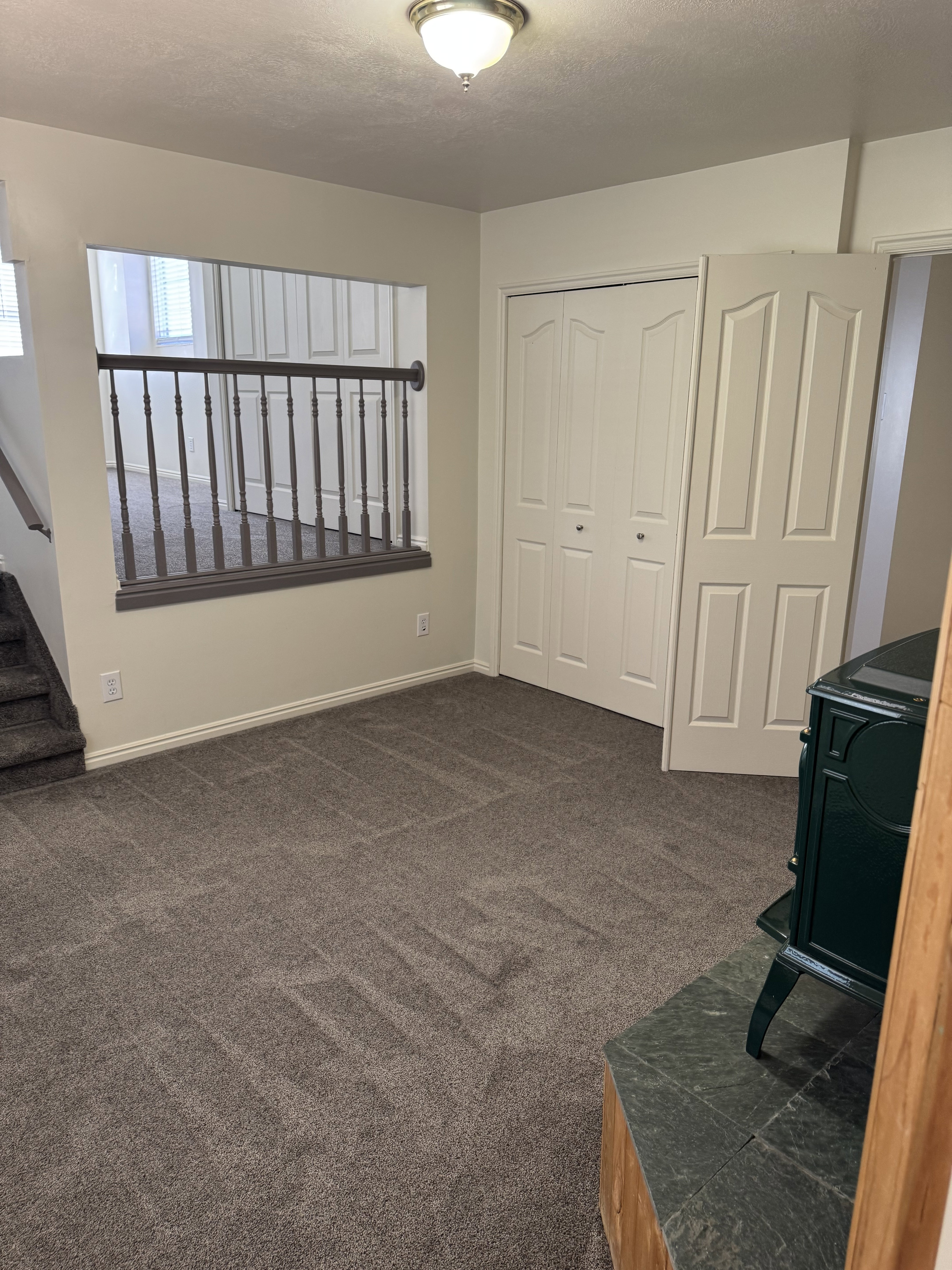 Carpeted interior space featuring a partial wall with a wood-tone railing and a built-in wood stove with a stone-tile base