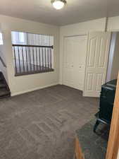Carpeted interior space featuring a partial wall with a wood-tone railing and a built-in wood stove with a stone-tile base