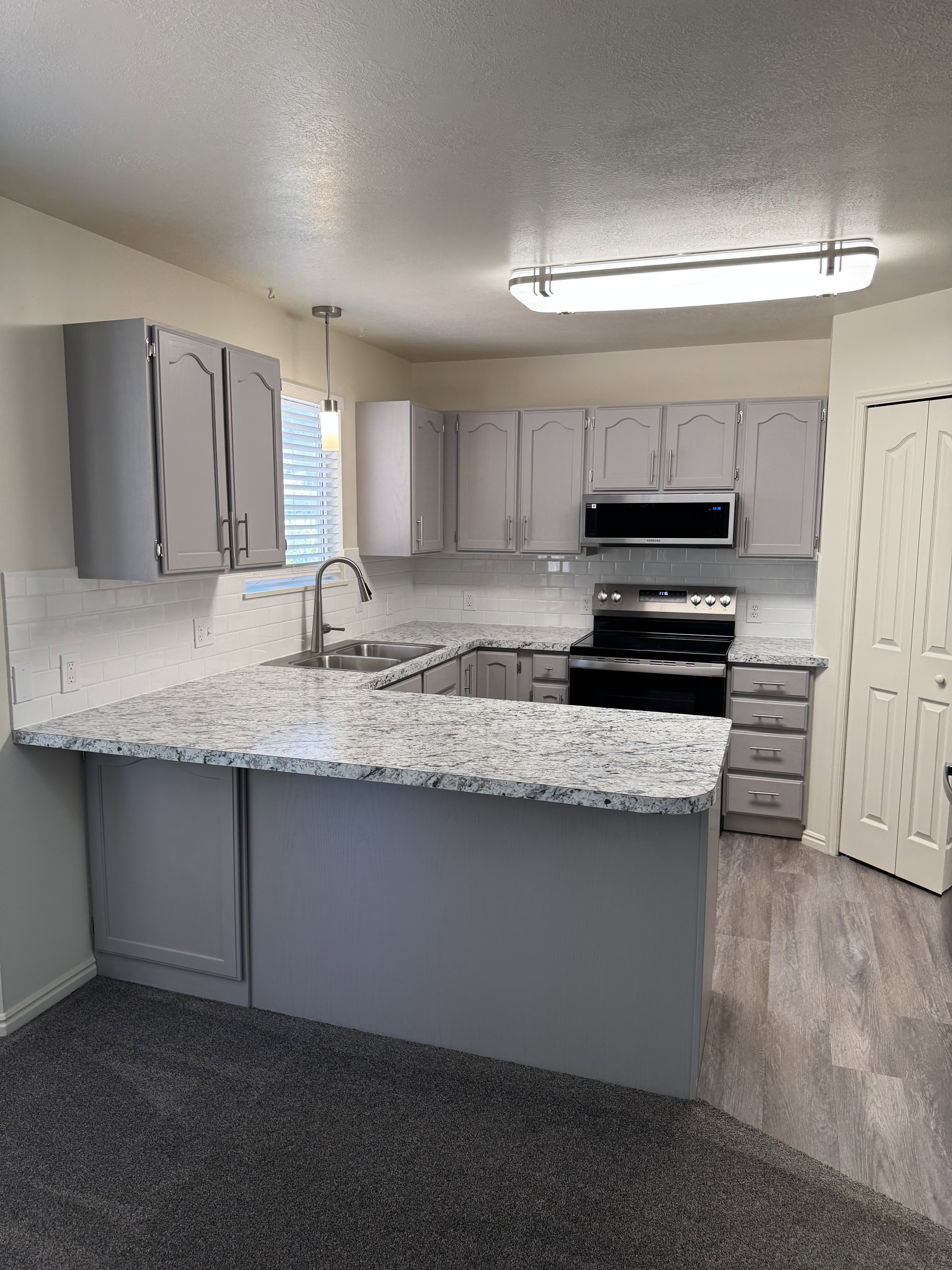 Kitchen featuring gray cabinetry, white subway tile backsplash, and light-toned countertops