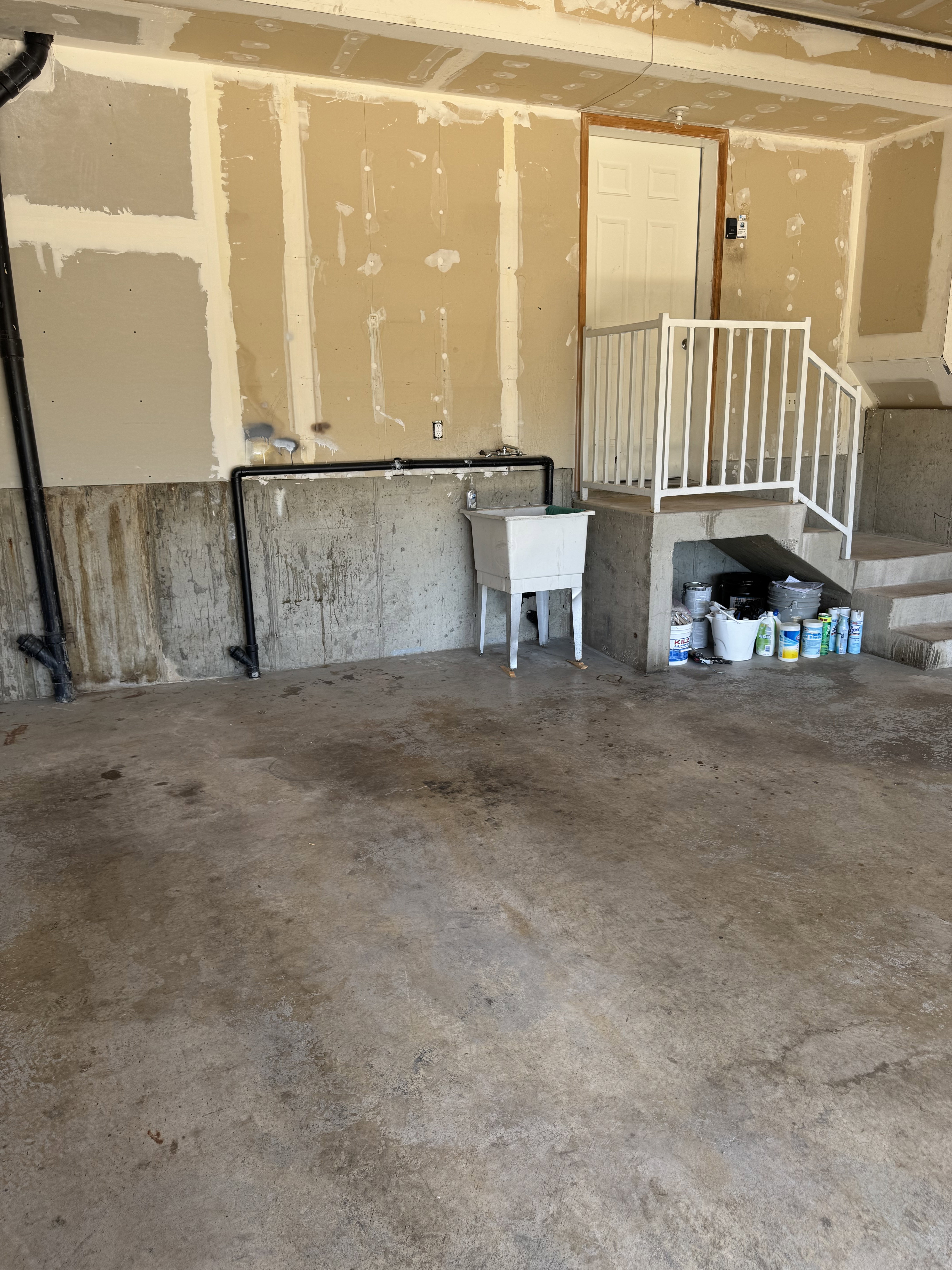 Concrete floor garage with utility sink, raised interior entry door, and white railing