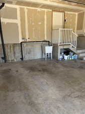 Concrete floor garage with utility sink, raised interior entry door, and white railing