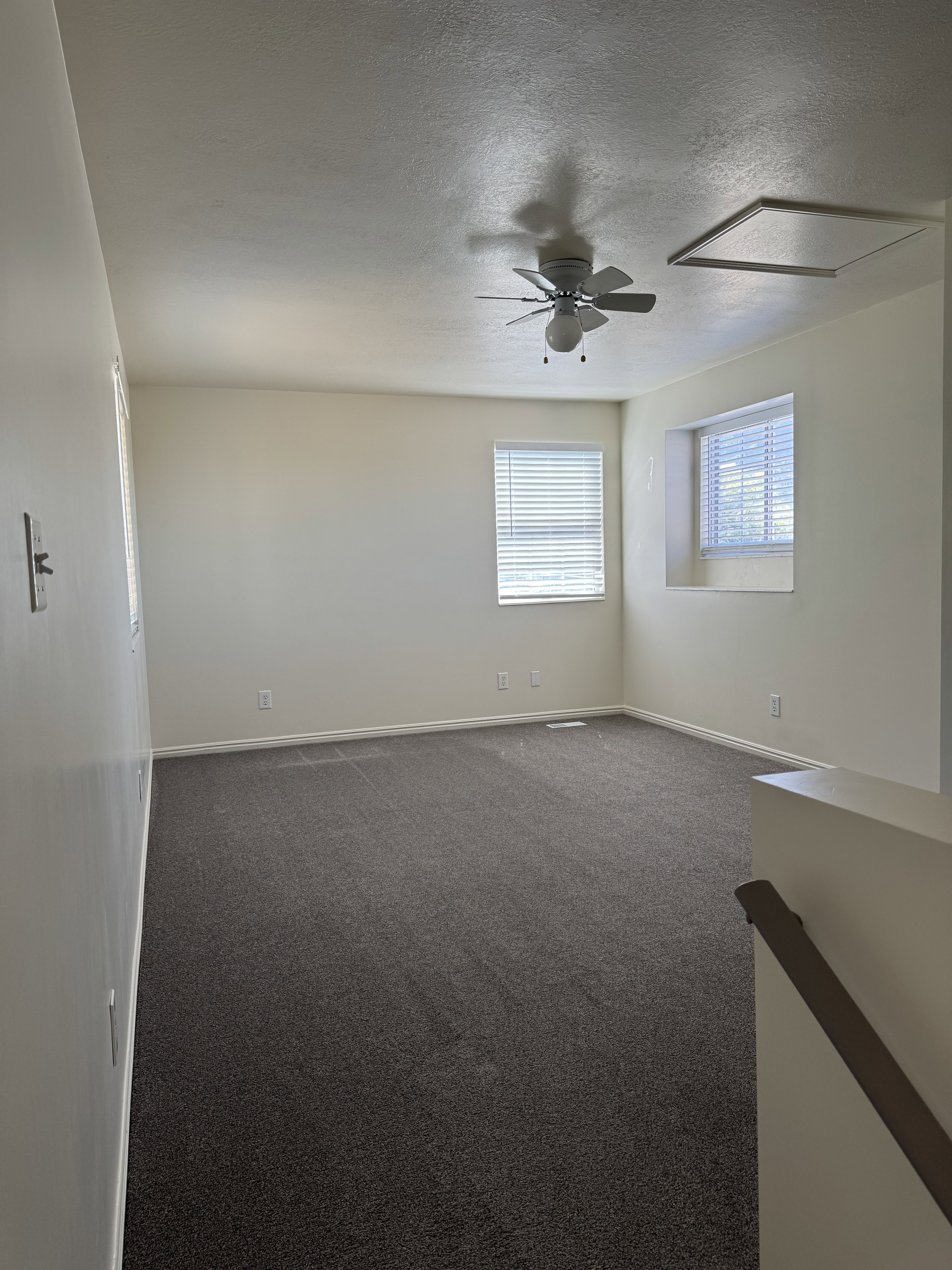 Carpeted room featuring multiple windows with blinds, a ceiling fan with integrated lighting, and neutral wall tones