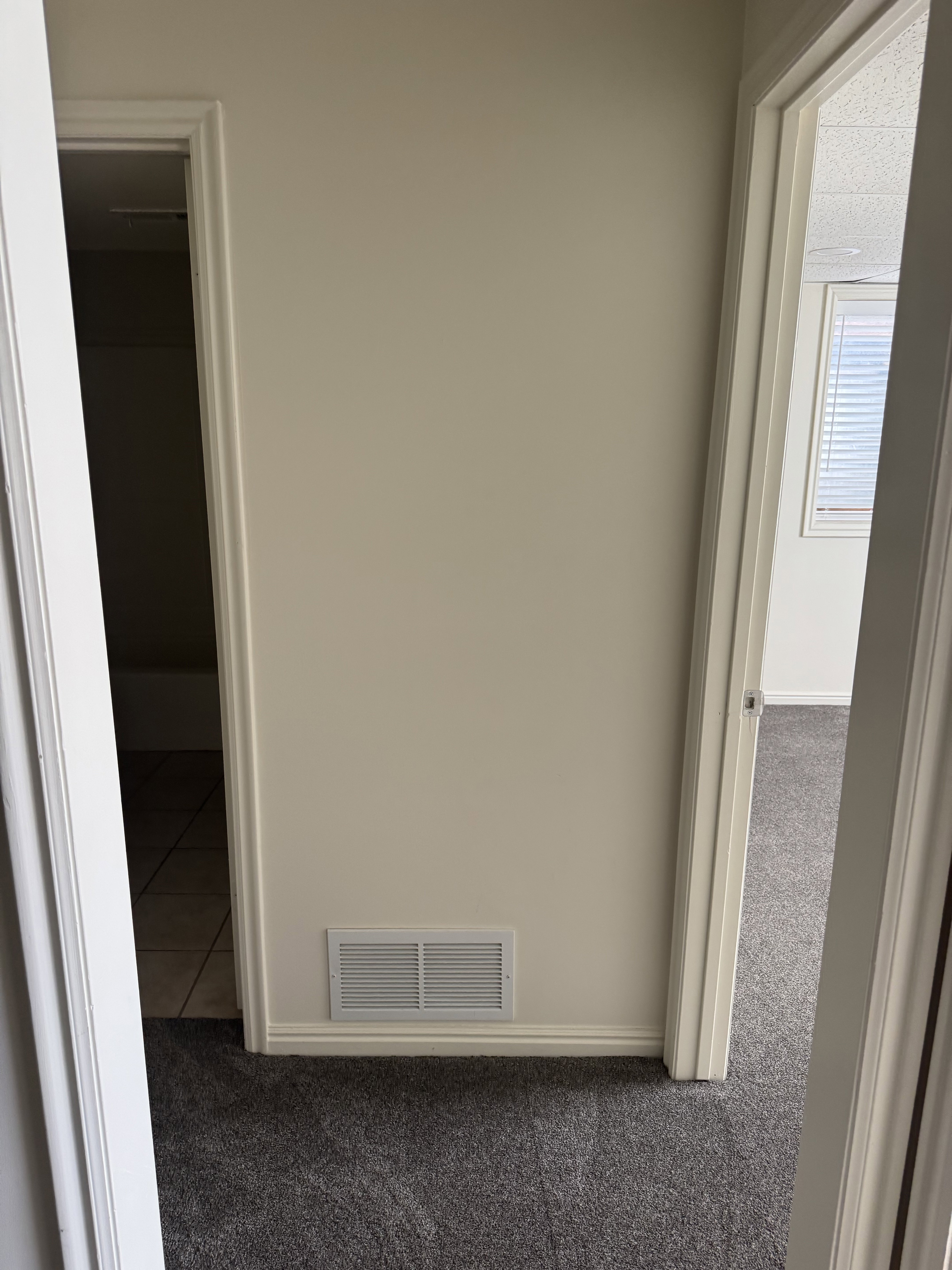 Wall with baseboard trim and a floor-level vent, flanked by two doorways