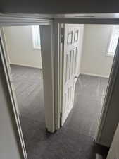 Corridor with neutral wall paint and gray carpeting, featuring two doorways with white trim and paneled doors