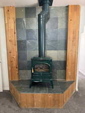 Freestanding green fireplace with an exposed flue, set against a slate tile wall