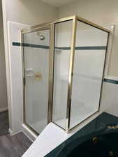 Gold-framed glass shower enclosure with a built-in shelf, white tile walls, a green accent tile band, and a coordinating green corner tub with brass fixtures