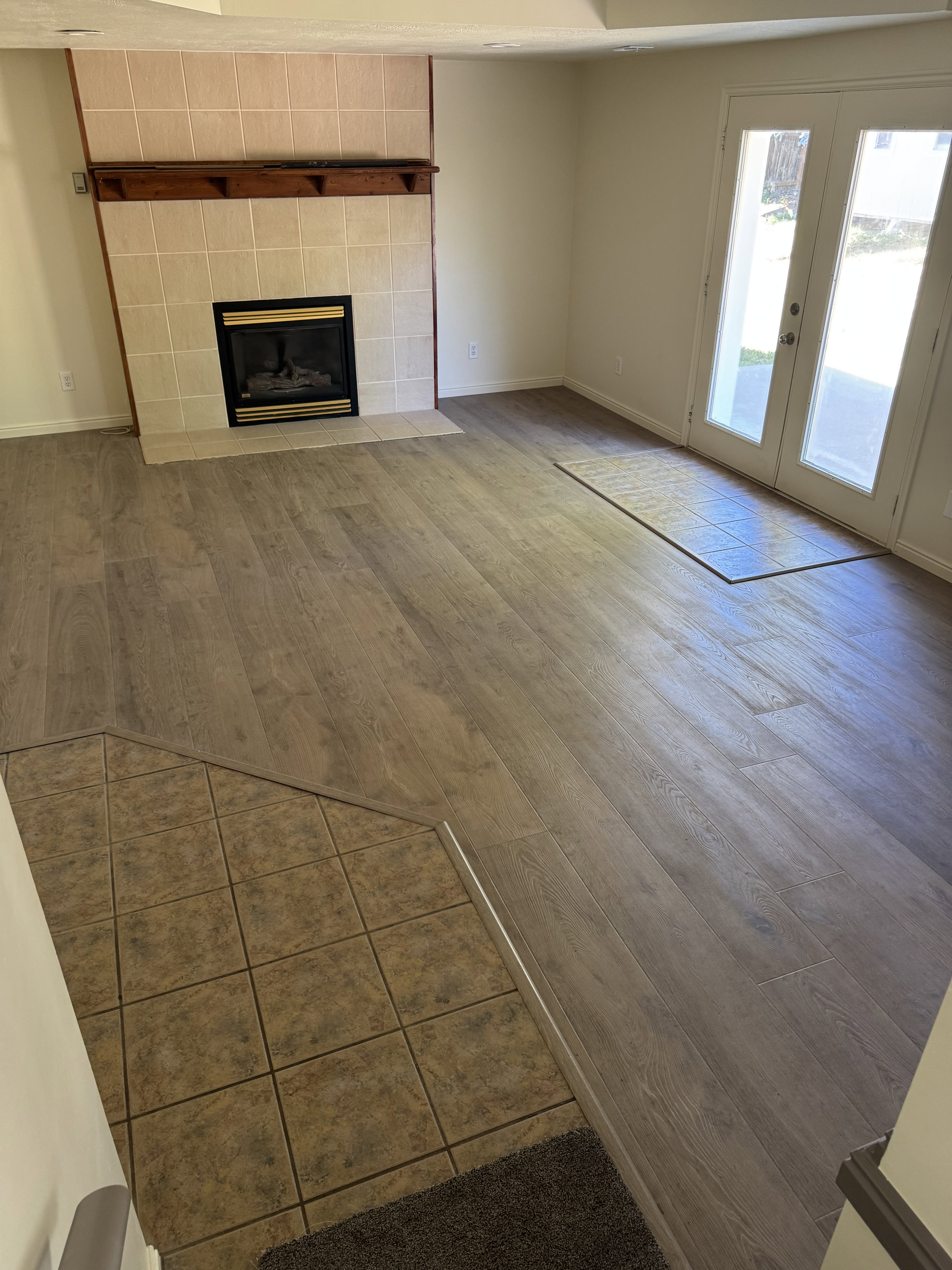 Spacious living area featuring a tiled fireplace with a wood mantle, wood-finish flooring, and double glass-paneled doors leading to an outdoor patio