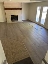 Spacious living area featuring a tiled fireplace with a wood mantle, wood-finish flooring, and double glass-paneled doors leading to an outdoor patio