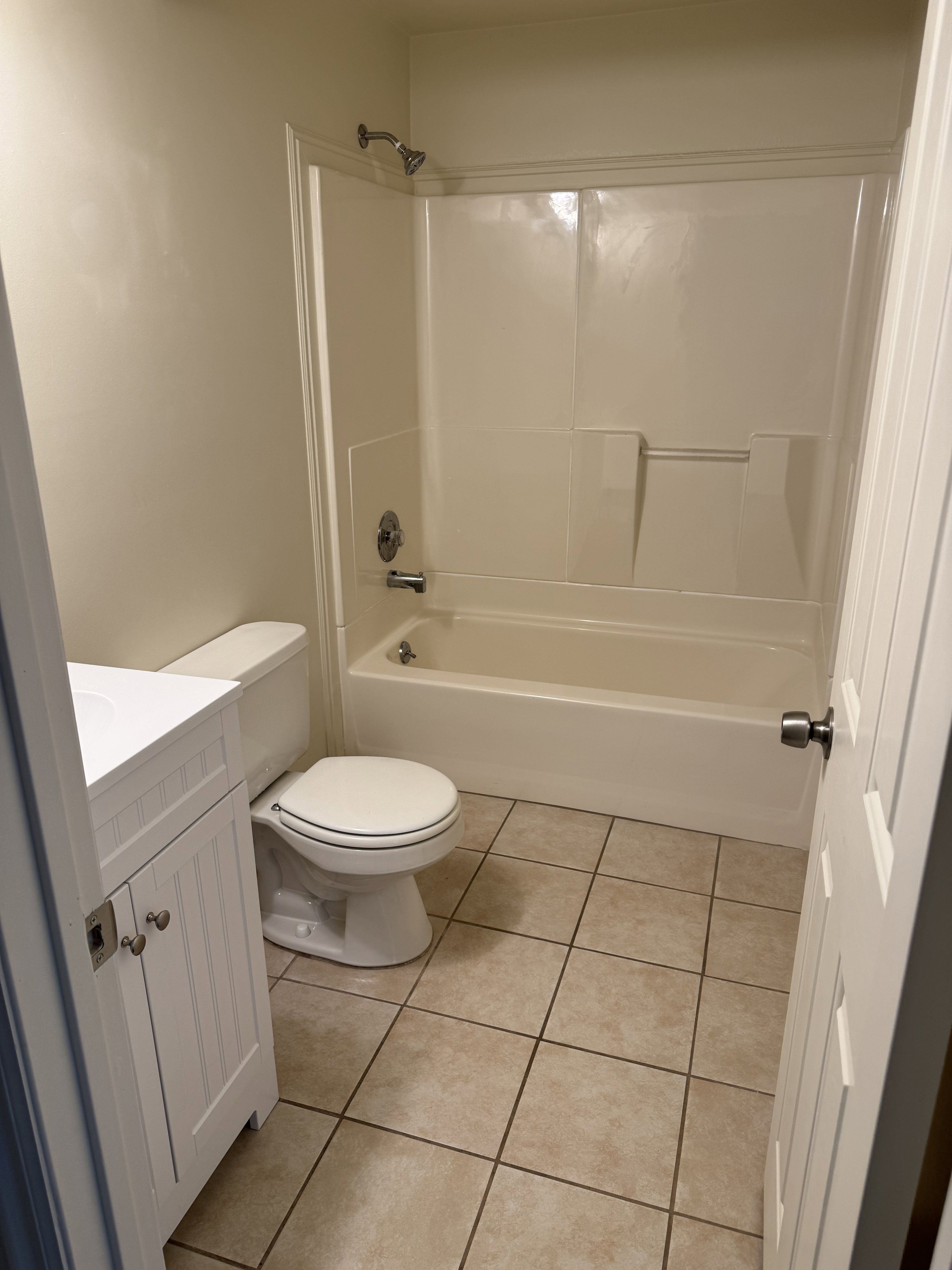 Bathroom featuring a white vanity with paneled doors, a white toilet, a bathtub with an integrated shower, and neutral-toned floor tiling