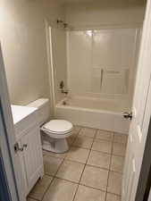 Bathroom featuring a white vanity with paneled doors, a white toilet, a bathtub with an integrated shower, and neutral-toned floor tiling