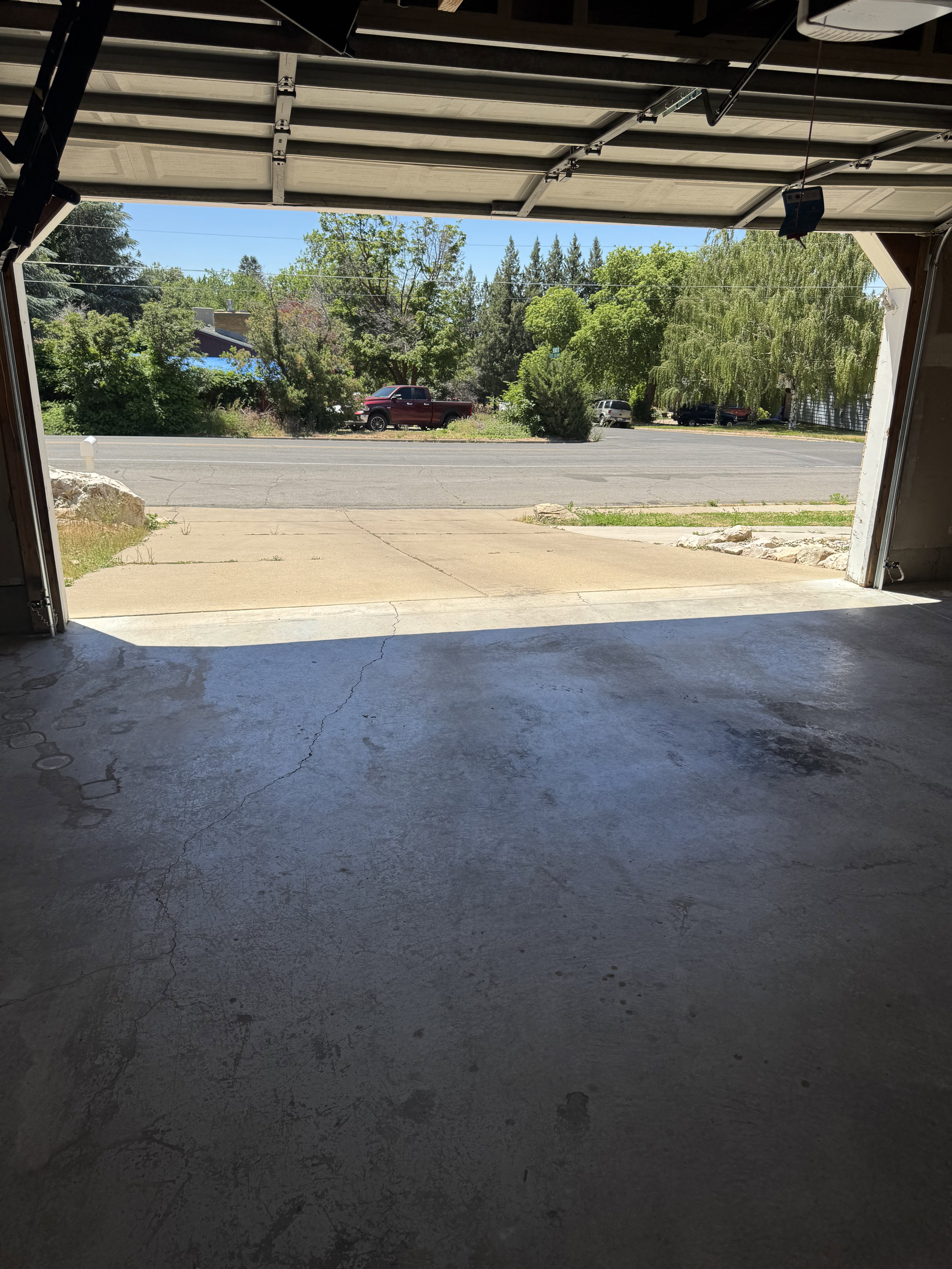 Garage interior with a concrete floor and an open overhead door, offering access to the exterior drive and street