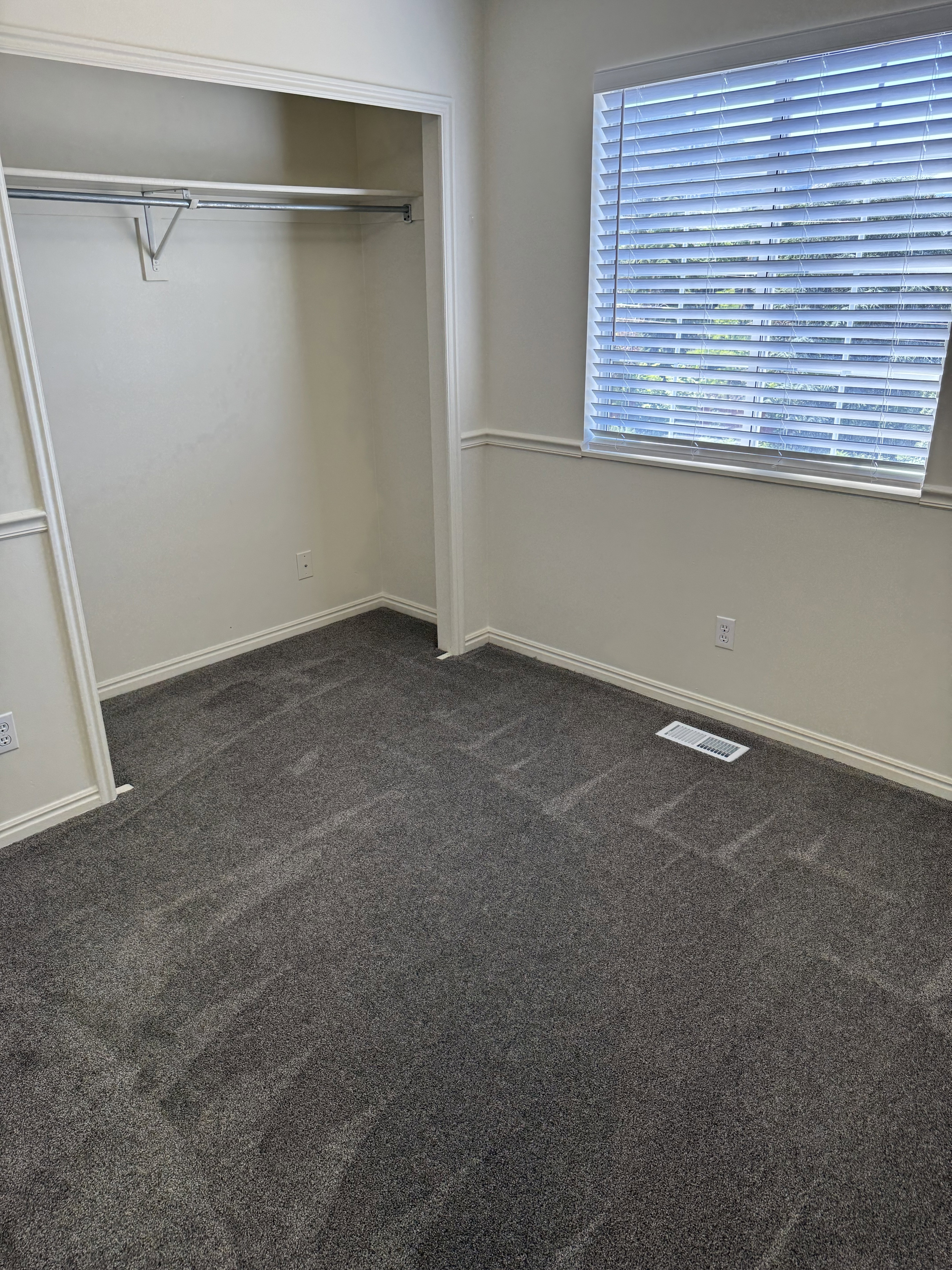 Interior room featuring plush gray carpeting, white walls, and a window with blinds