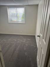 Room with light gray wall paint, gray carpet, a white framed window with blinds, and a white paneled door