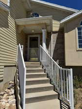 Inviting entryway featuring a covered porch, durable concrete steps, white metal railings, a half-round transom window, and a combination of siding and brick facade
