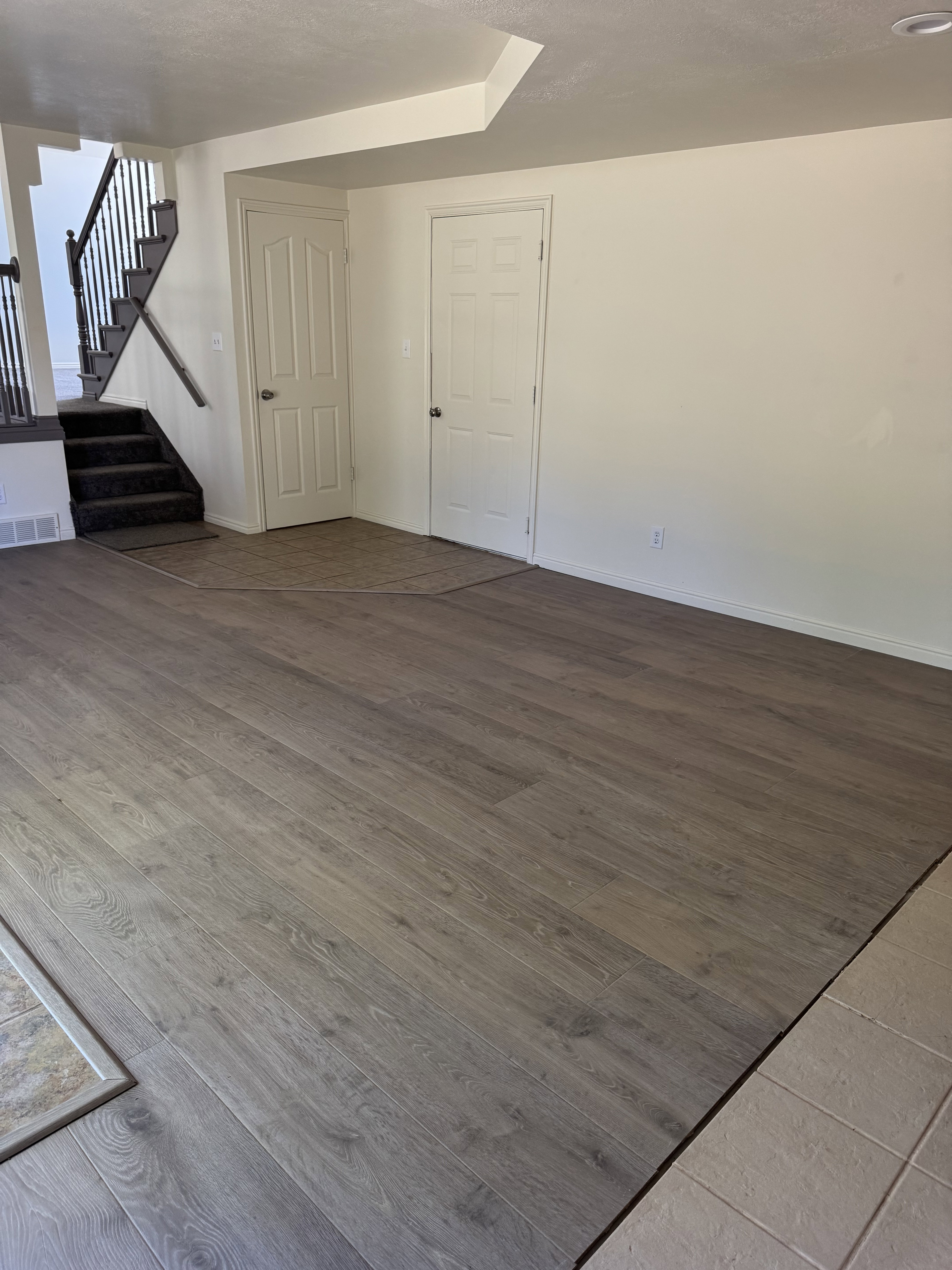 Spacious interior featuring wood-finish flooring, a carpeted staircase with a dark wrought iron railing, and neutral wall tones