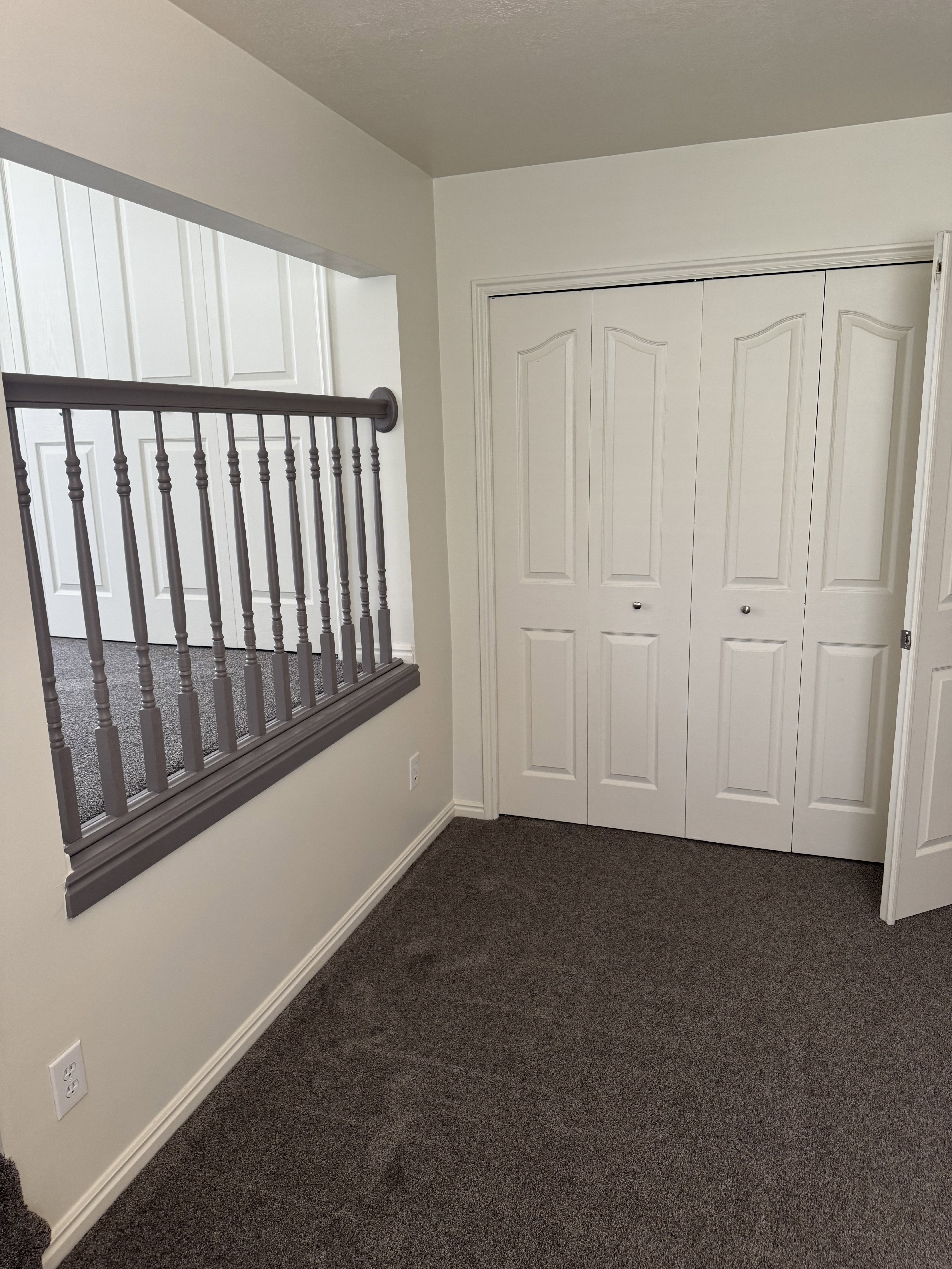 Carpeted space with bi-fold closet doors, white baseboards, and a dark gray balustrade