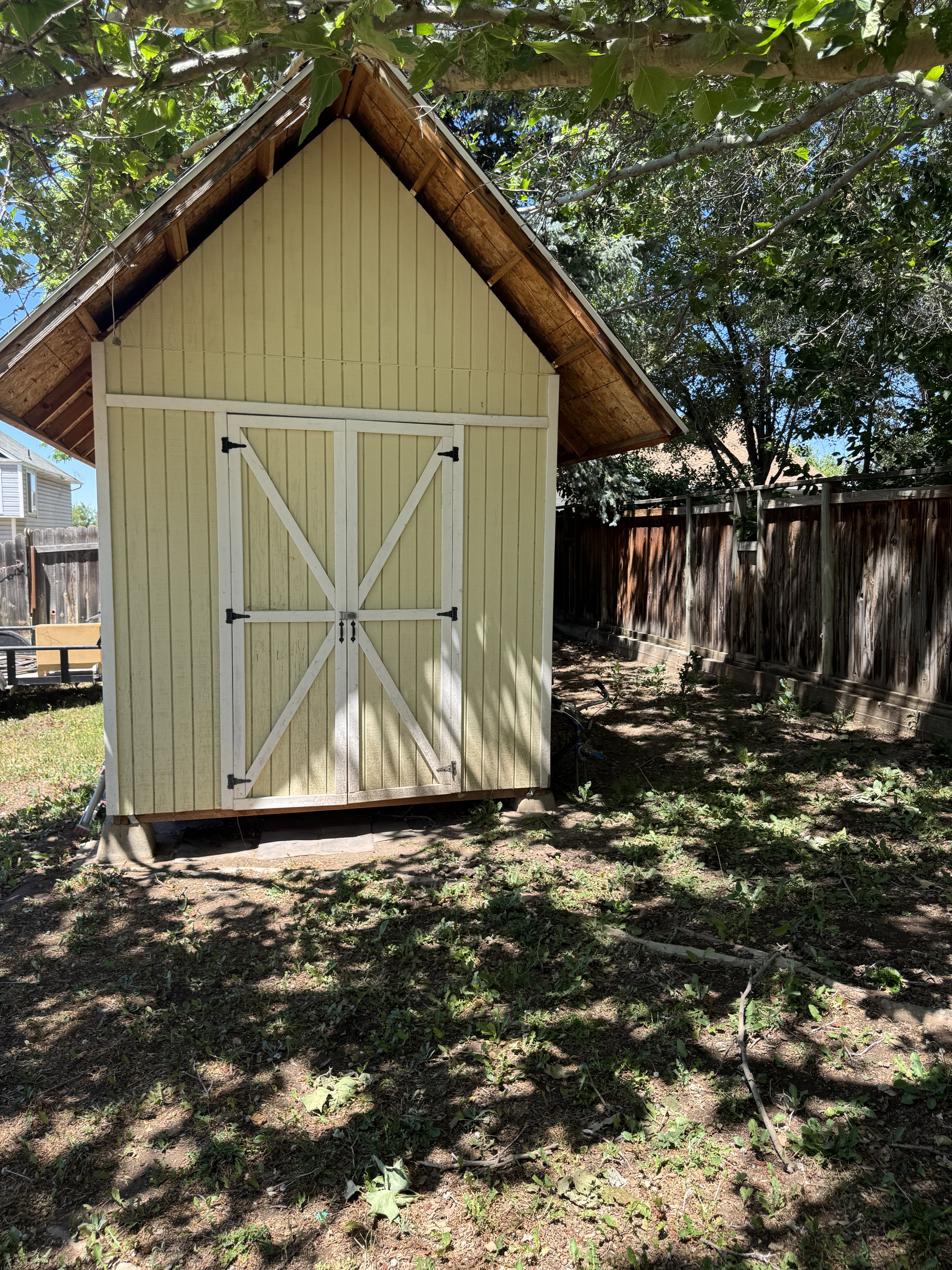Gable-roof storage shed with light yellow siding and white double doors featuring cross-buck detailing