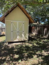 Gable-roof storage shed with light yellow siding and white double doors featuring cross-buck detailing