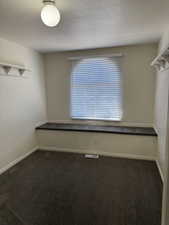Room featuring a window with blinds, a built-in window seat, dark grey carpeting, a ceiling-mounted light fixture, and white wall shelving
