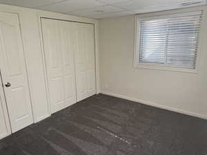 Neutral-toned interior featuring grey carpet flooring, a window with horizontal blinds, and paneled bifold closet doors