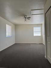 Spacious room featuring neutral carpeting, two windows with blinds, a ceiling fan with integrated lighting, and a white bi-fold closet door